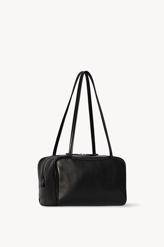 The Row Astra Bag in black, angled view showing the side zip, flat base and embossed The Row stamp