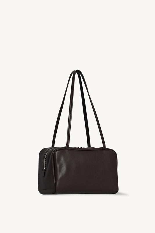 The Row Astra Bag in dark brown, angled view showing the side zip and embossed The Row stamp