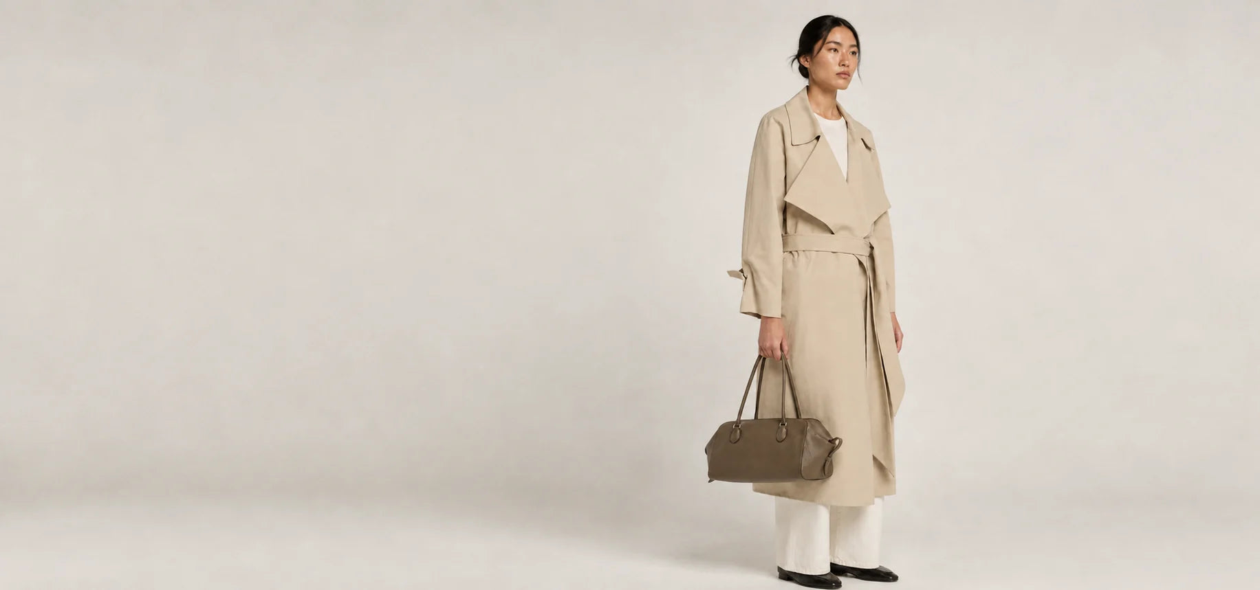 Model in a neutral trench coat carrying a brown leather bag
