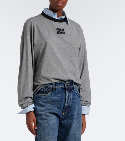 Miu Miu Oversized Cotton Jersey T-Shirt in grey worn over a blue shirt with jeans, front angle