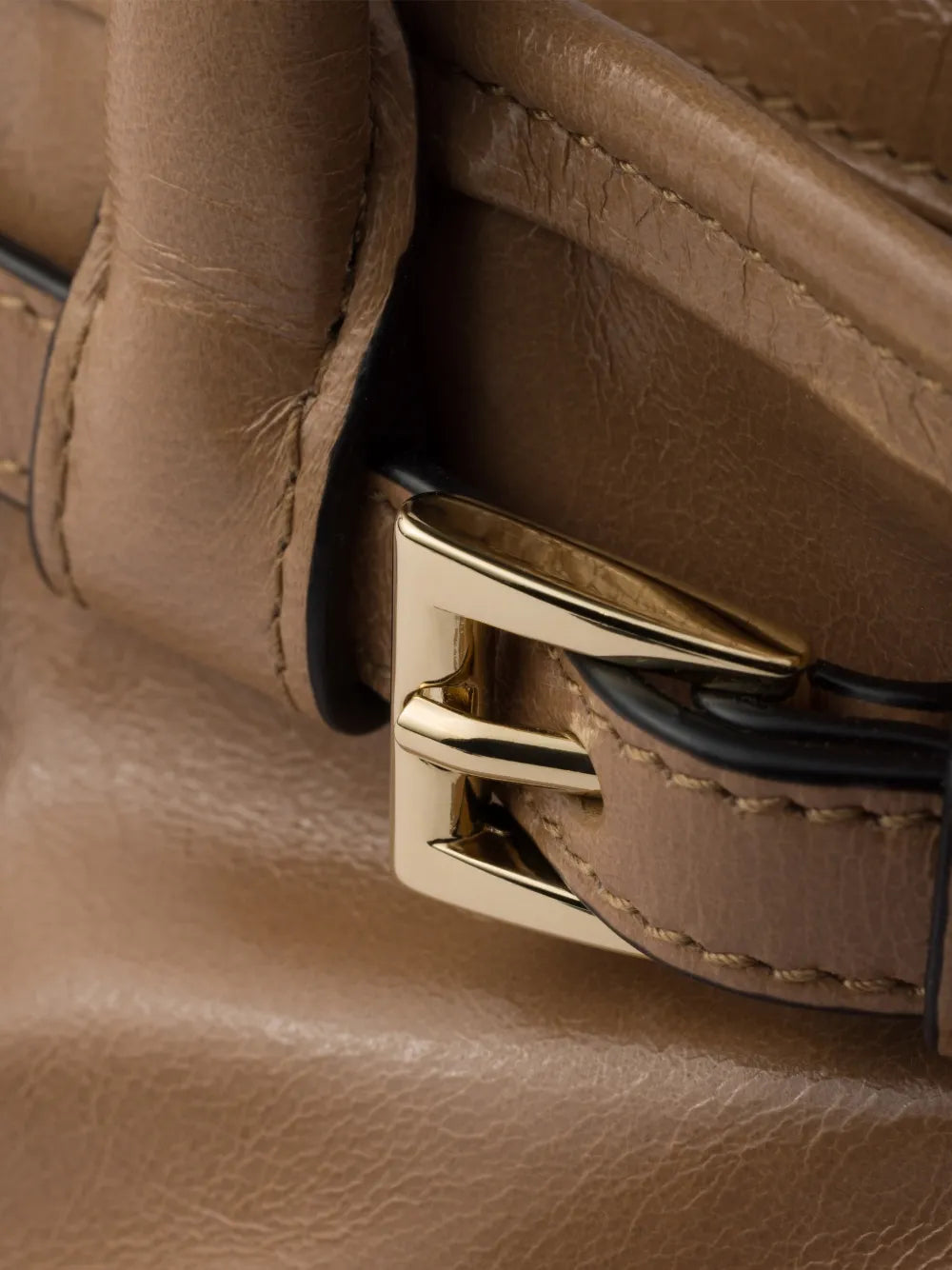 Prada Bonnie handbag close-up of polished gold buckle on the tan leather front belt strap