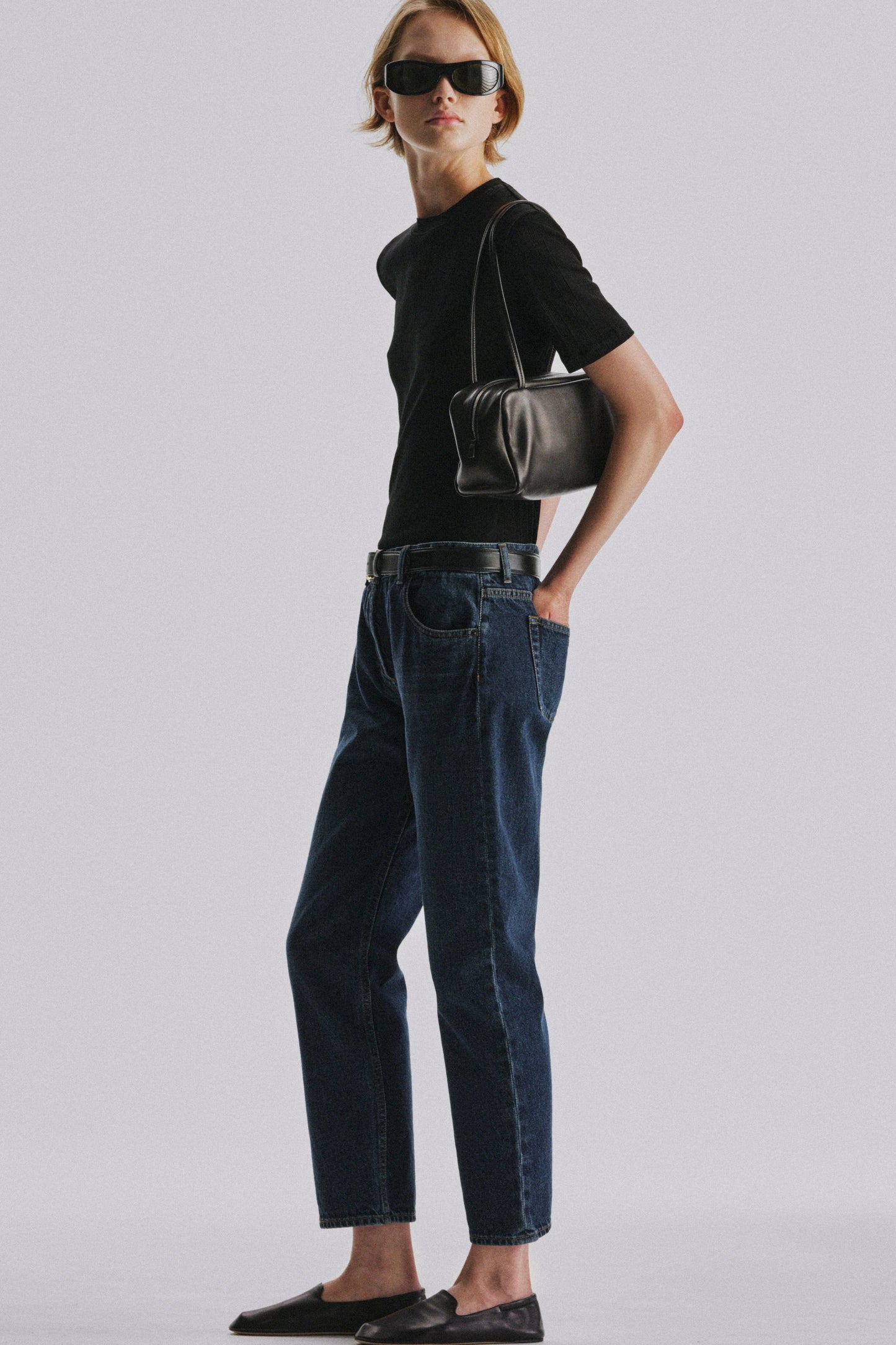 The Row Astra Bag in black worn on the shoulder by a model in a black tee and dark denim