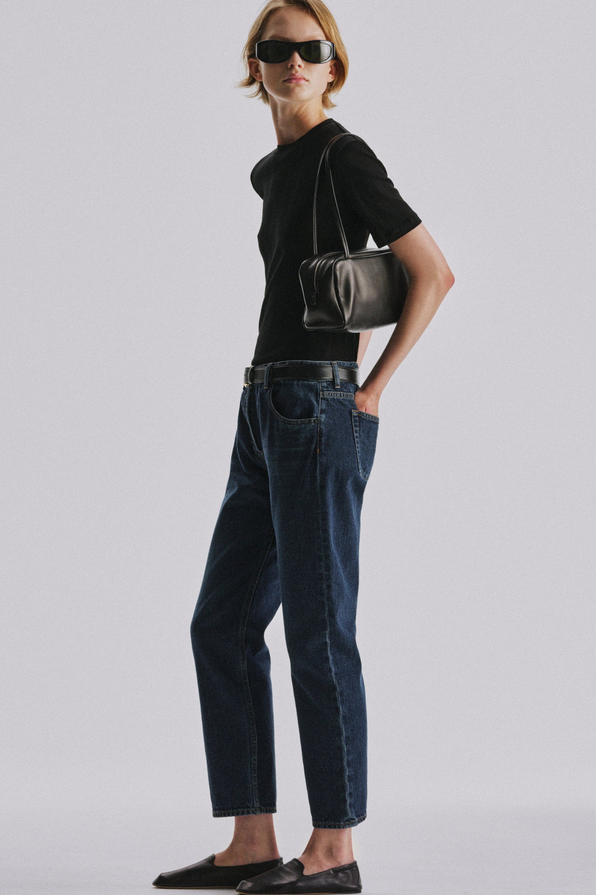 The Row Astra Bag in black worn on the shoulder by a model in a black tee and dark denim