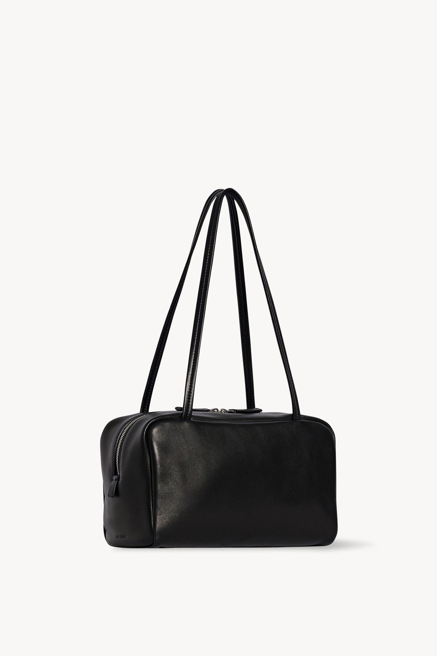 The Row Astra Bag in black, angled view showing the side zip, flat base and embossed The Row stamp