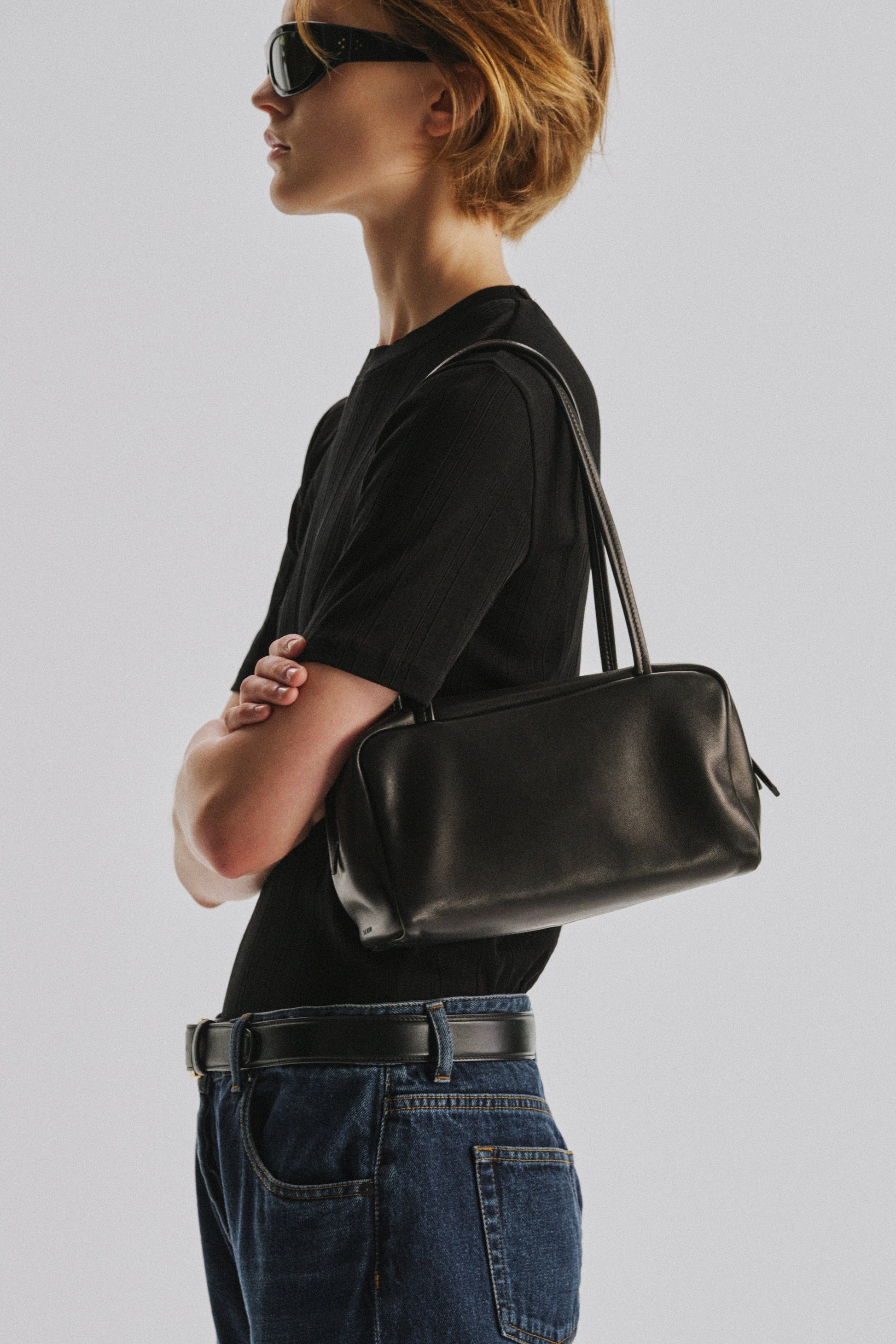 The Row Astra Bag in black carried on the shoulder, close view of the glossy lambskin body