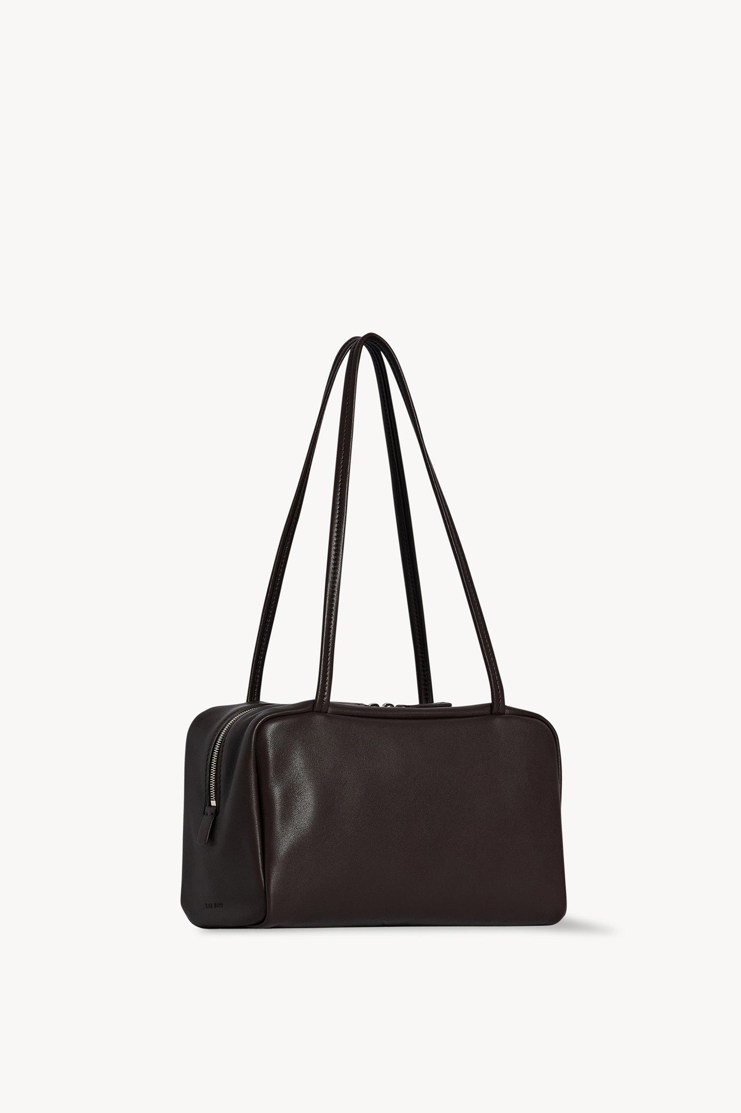 The Row Astra Bag in dark brown, angled view showing the side zip and embossed The Row stamp