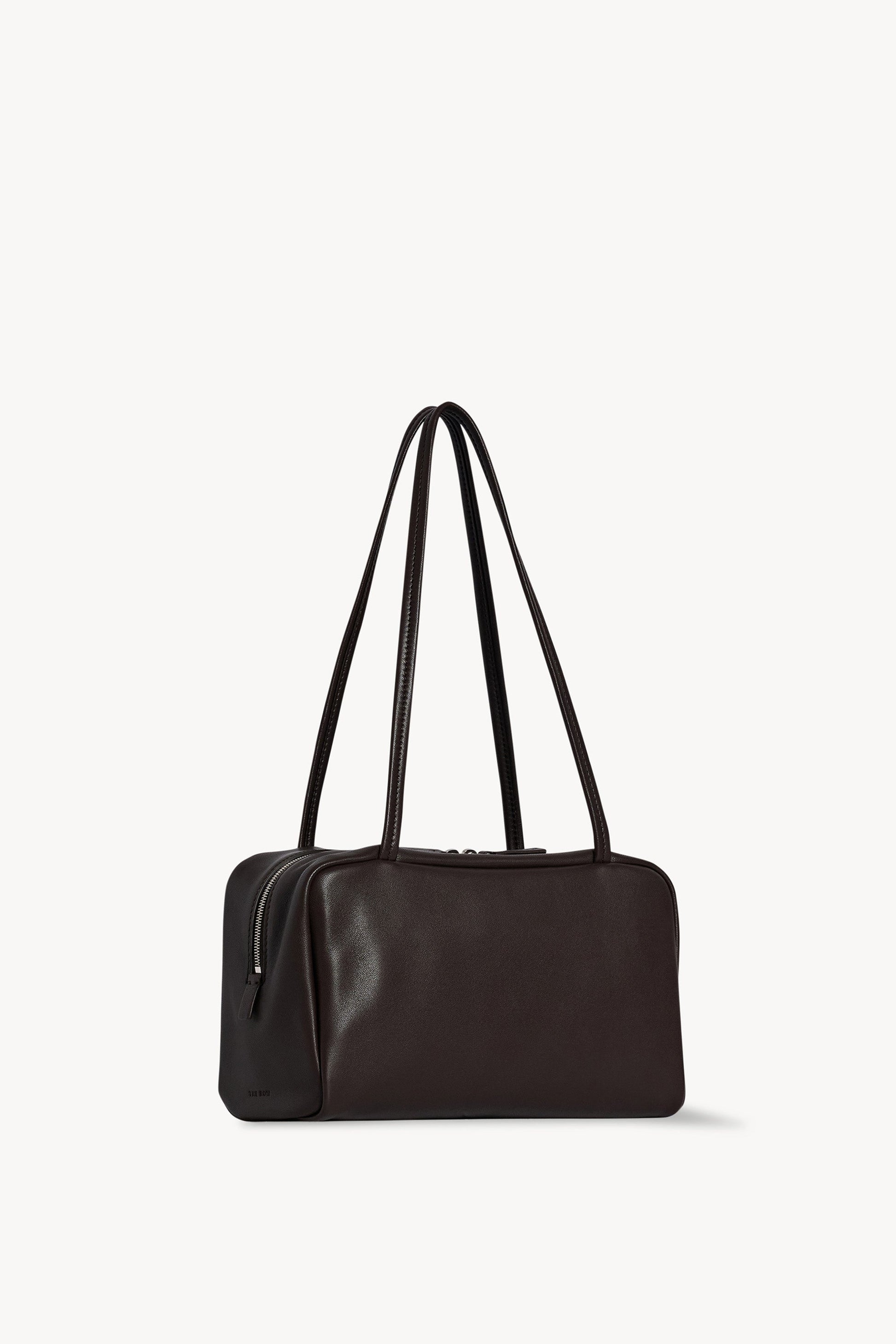 The Row Astra Bag in dark brown, angled view showing the side zip and embossed The Row stamp