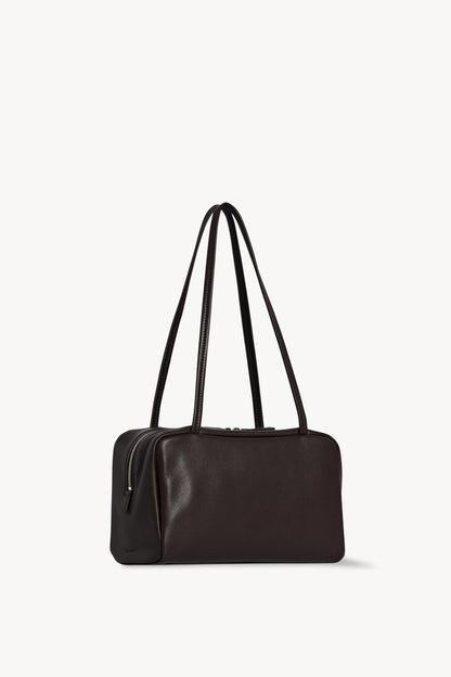 The Row Astra Bag in dark brown, angled view showing the side zip and embossed The Row stamp