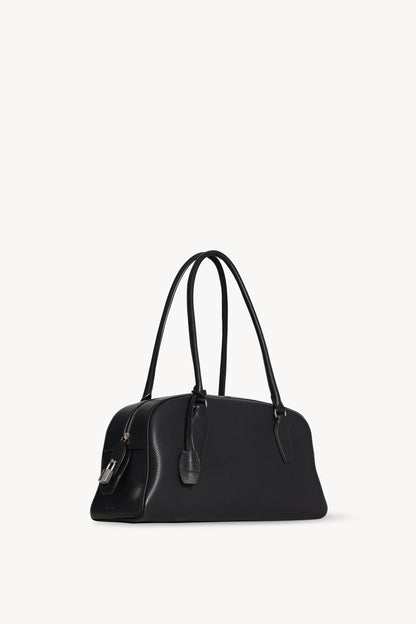 The Row E/W India Bag in black, three-quarter angle showing the top zip, padlock and leather key holder