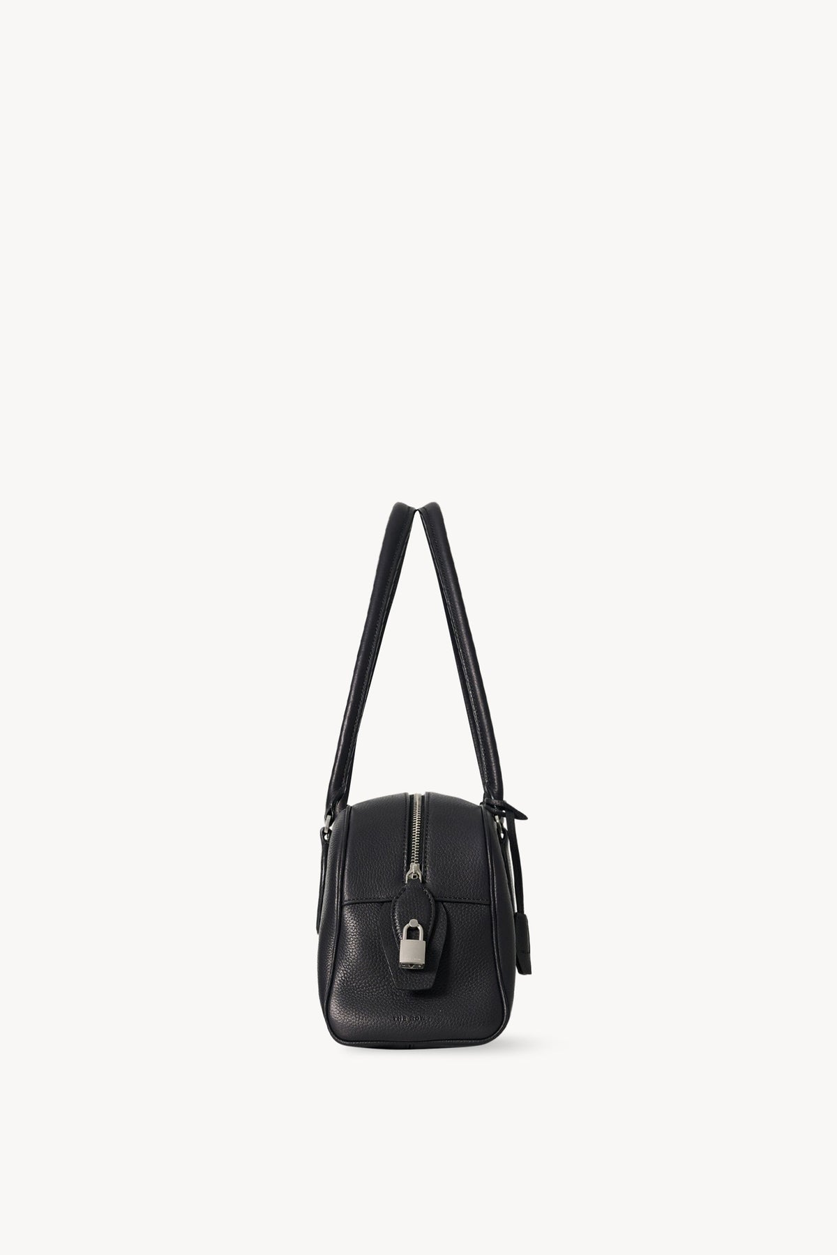 The Row E/W India Bag in black, end-on side view of the top zip, padlock and piped seams