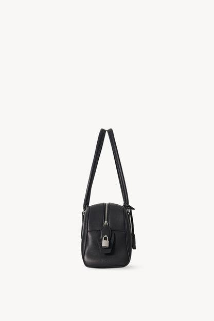 The Row E/W India Bag in black, end-on side view of the top zip, padlock and piped seams