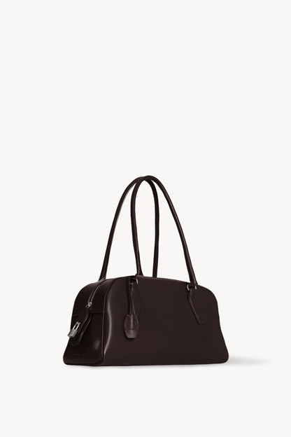 The Row E/W India Bag in dark brown, three-quarter angle showing the top zip and metal padlock