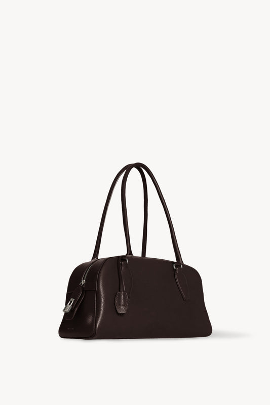 The Row E/W India Bag in dark brown, three-quarter angle showing the top zip and metal padlock