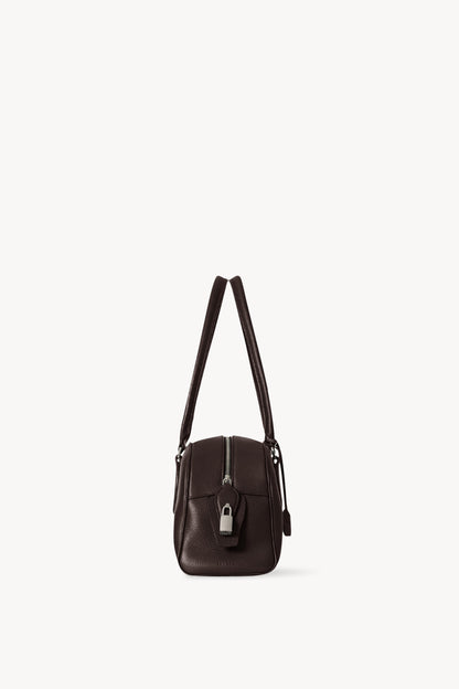 The Row E/W India Bag in dark brown, end-on side view with top zip and piped edges